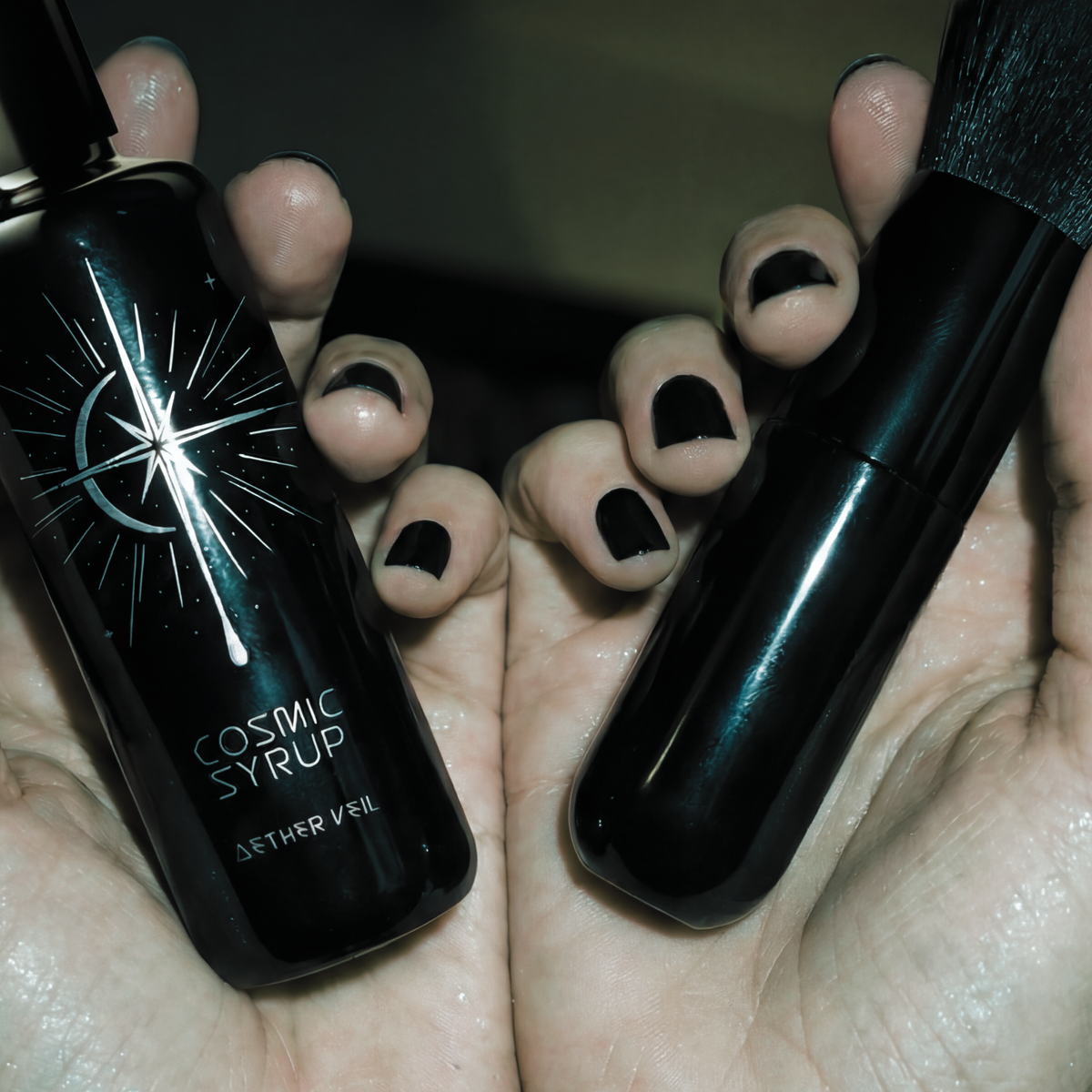 Cosmic Syrup shimmering dry body oil vessel and lumen applicator brush being held in the palm of hands with black finger nails early 2000s era.